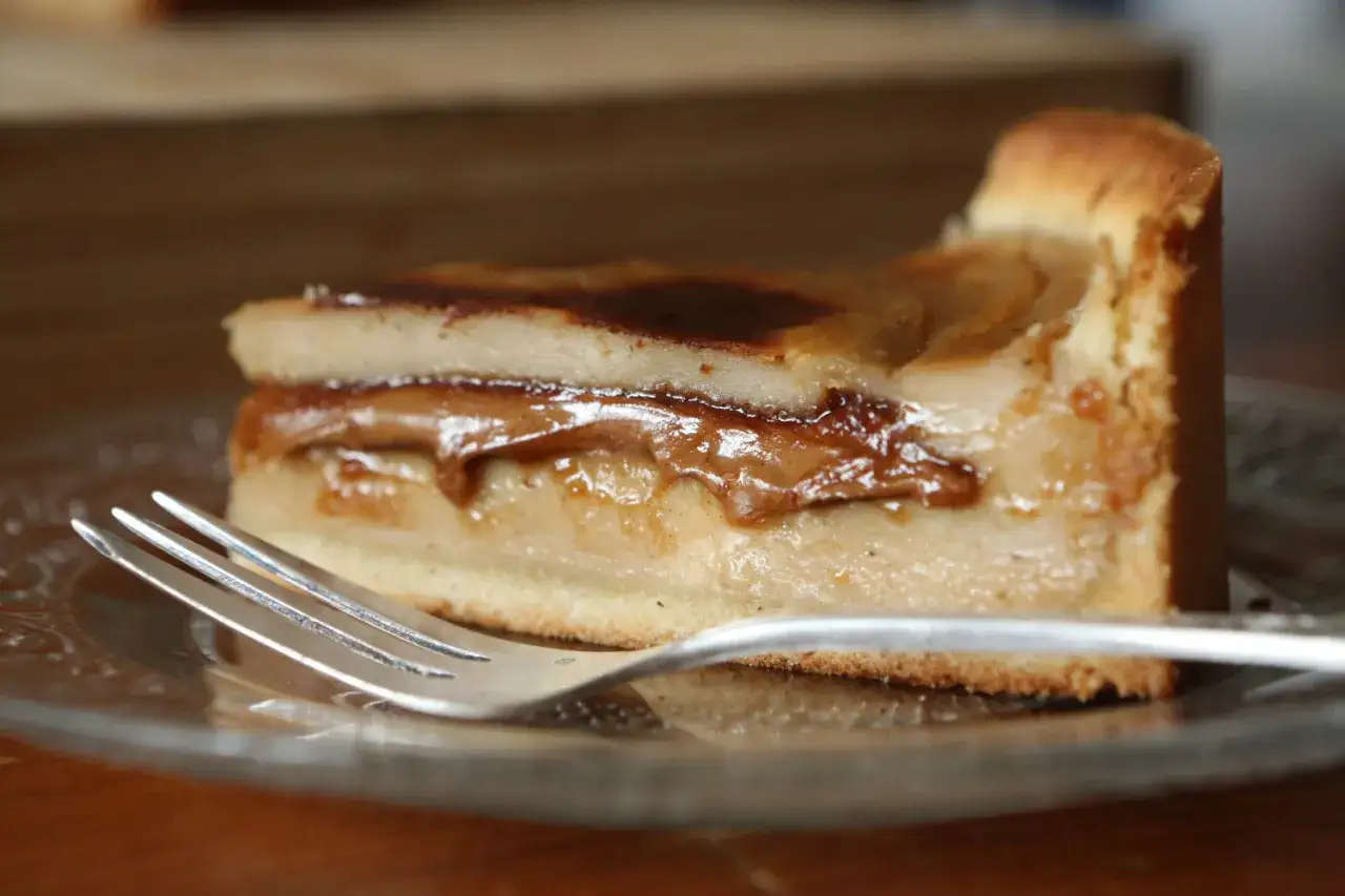 Une part de flan pralin&eacute; aux pommes, dor&eacute;e et gourmande, sur une assiette avec une fourchette.