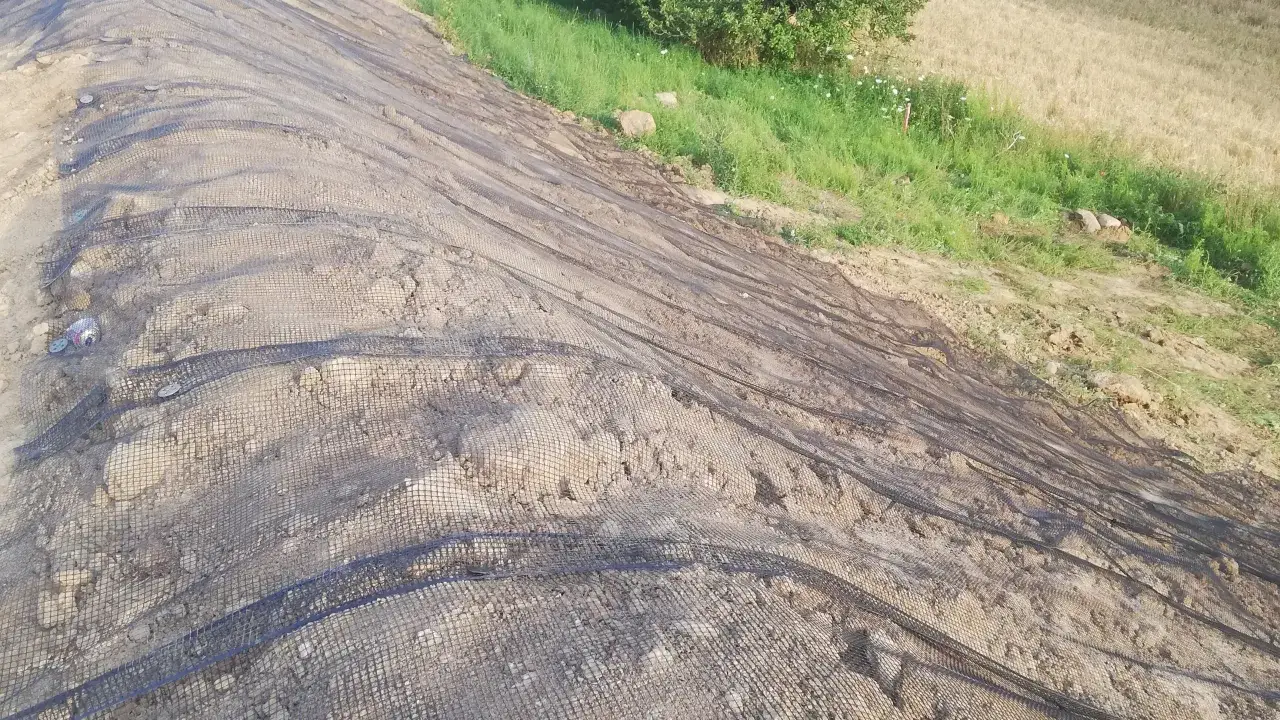 Siatka geotechniczna na skarpie, która może posłużyć do umocnienia gruntu i zapobiegania erozji. To rozwiązanie, czym wyłożyć rów melioracyjny, by był stabilny.