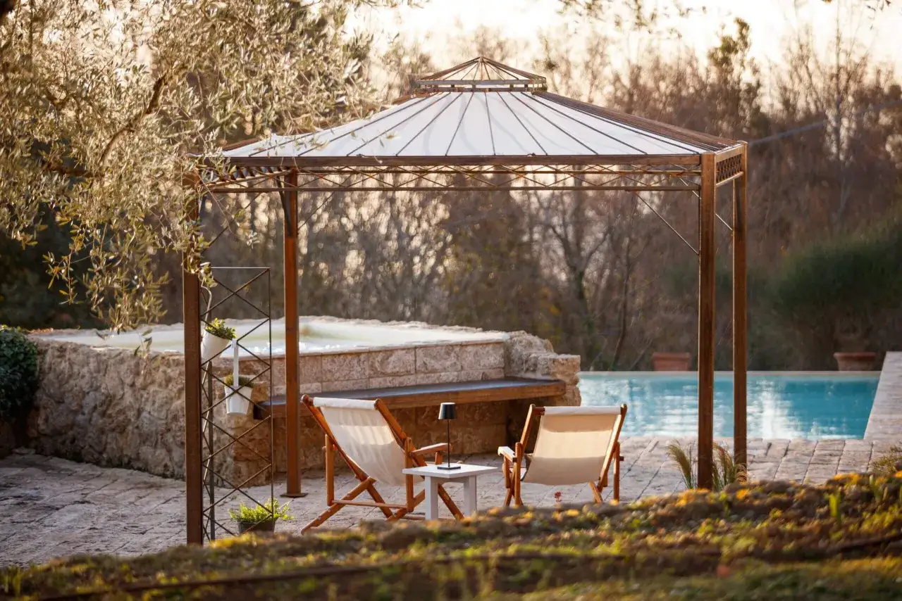 Gem&uuml;tliche Sitzecken im Garten laden zum Entspannen ein. Ein Pavillon &uuml;berspannt zwei Liegest&uuml;hle mit kleinem Tisch, daneben ein Pool und ein Whirlpool.