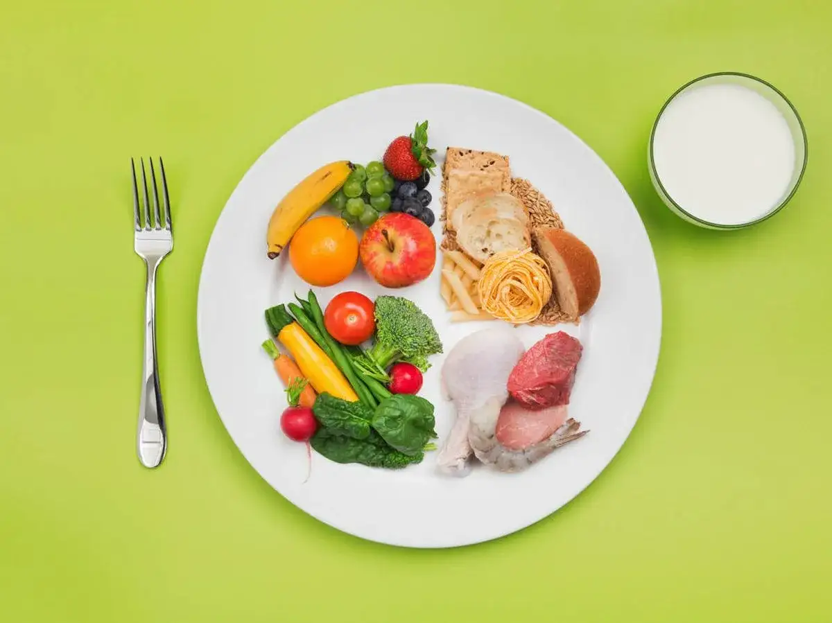Plato con variedad de alimentos bajos en calor&iacute;as: frutas, verduras, granos, prote&iacute;nas y un vaso de leche.