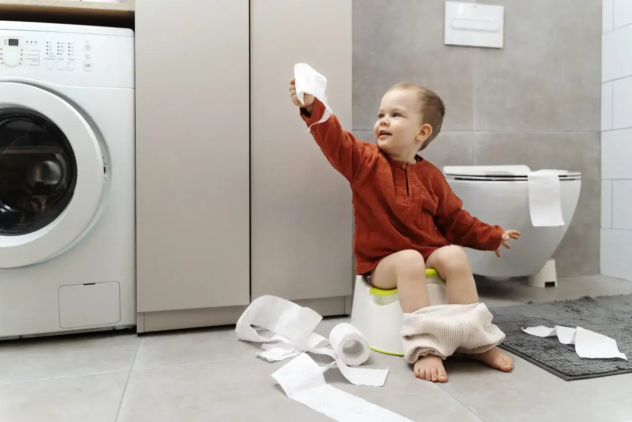 Ni&ntilde;o feliz en orinal, celebrando un paso importante en dejar el pa&ntilde;al. Papel higi&eacute;nico esparcido, s&iacute;mbolo de su progreso.