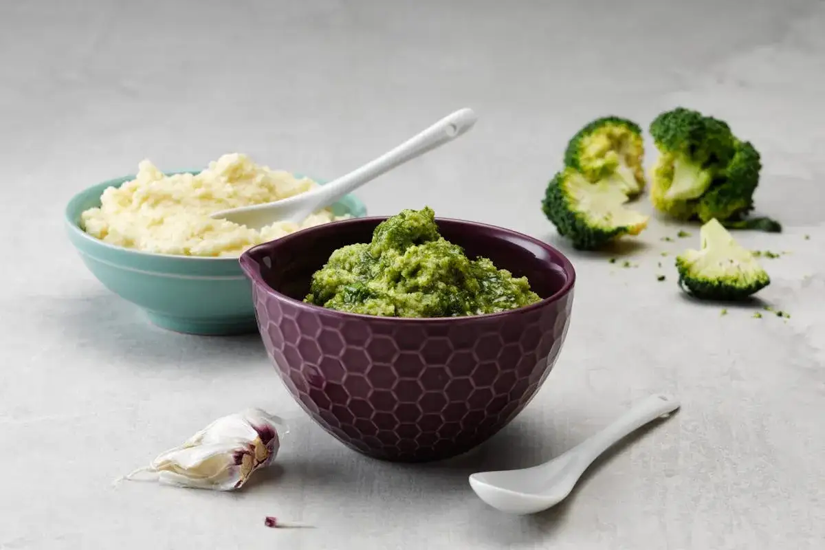 Grön broccoli-röra i skål, bredvid en skål med ljus puré. Broccoli är full av vitaminer.