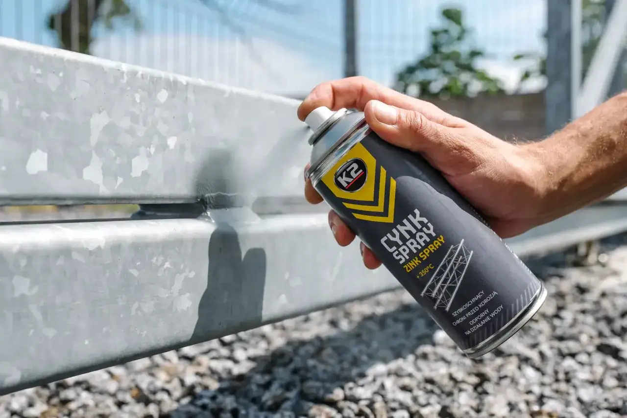 Ręka trzyma puszkę cynk sprayu, aplikując ją na metalową konstrukcję. Idealne rozwiązanie, czym zakonserwować podwozie przed rdzą.