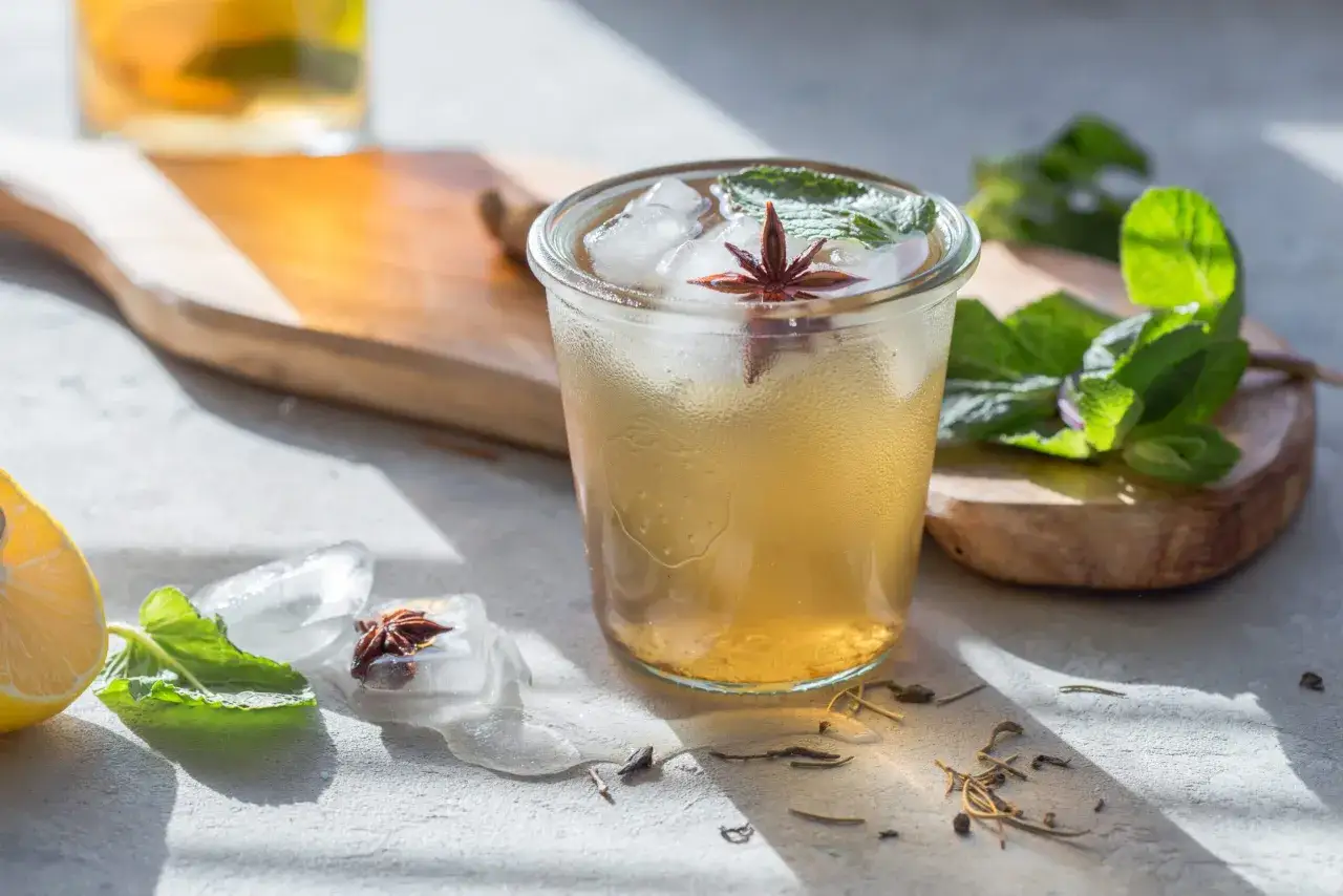 Un verre d'infusion à froid, garni de menthe et d'anis étoilé, avec des glaçons fondants et une tranche de citron.