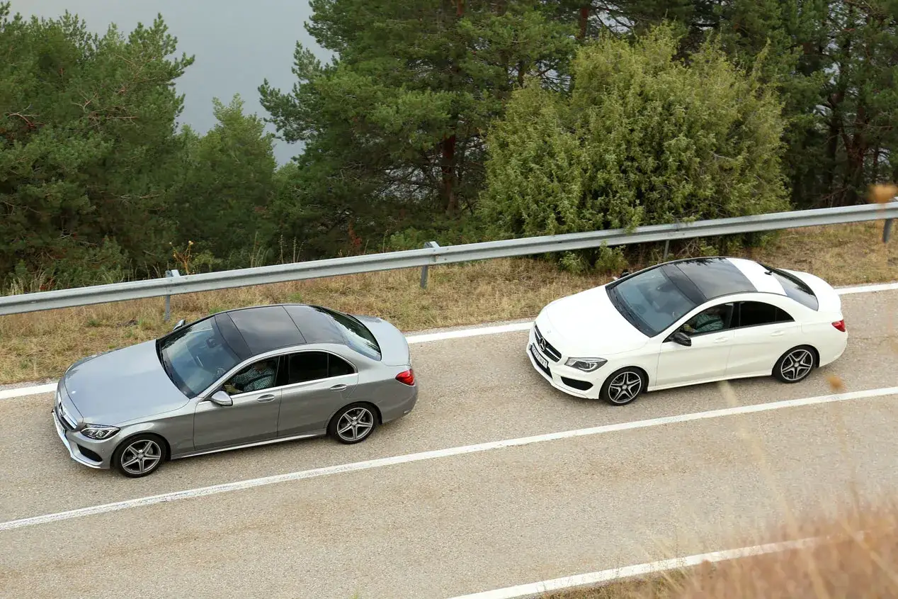 Dos Mercedes, un Clase C gris y un Clase E blanco, circulan por una carretera rodeada de &aacute;rboles.