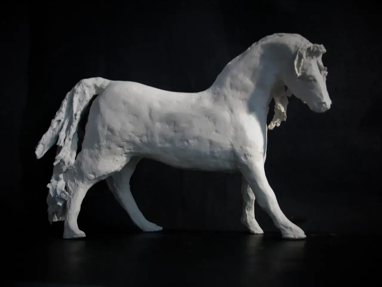 Białe figurki z papier mache przedstawiające konia w ruchu. Rzeźba ma dynamiczną postawę, z uniesioną głową i rozwianą grzywą.