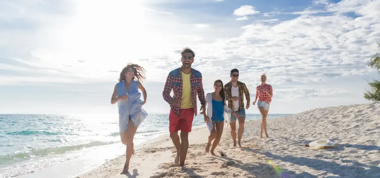 Radosna grupa przyjaciół biegnie po plaży, ciesząc się słońcem i morzem. Typowy Polak na wakacjach w pełni korzysta z wolności i beztroski.