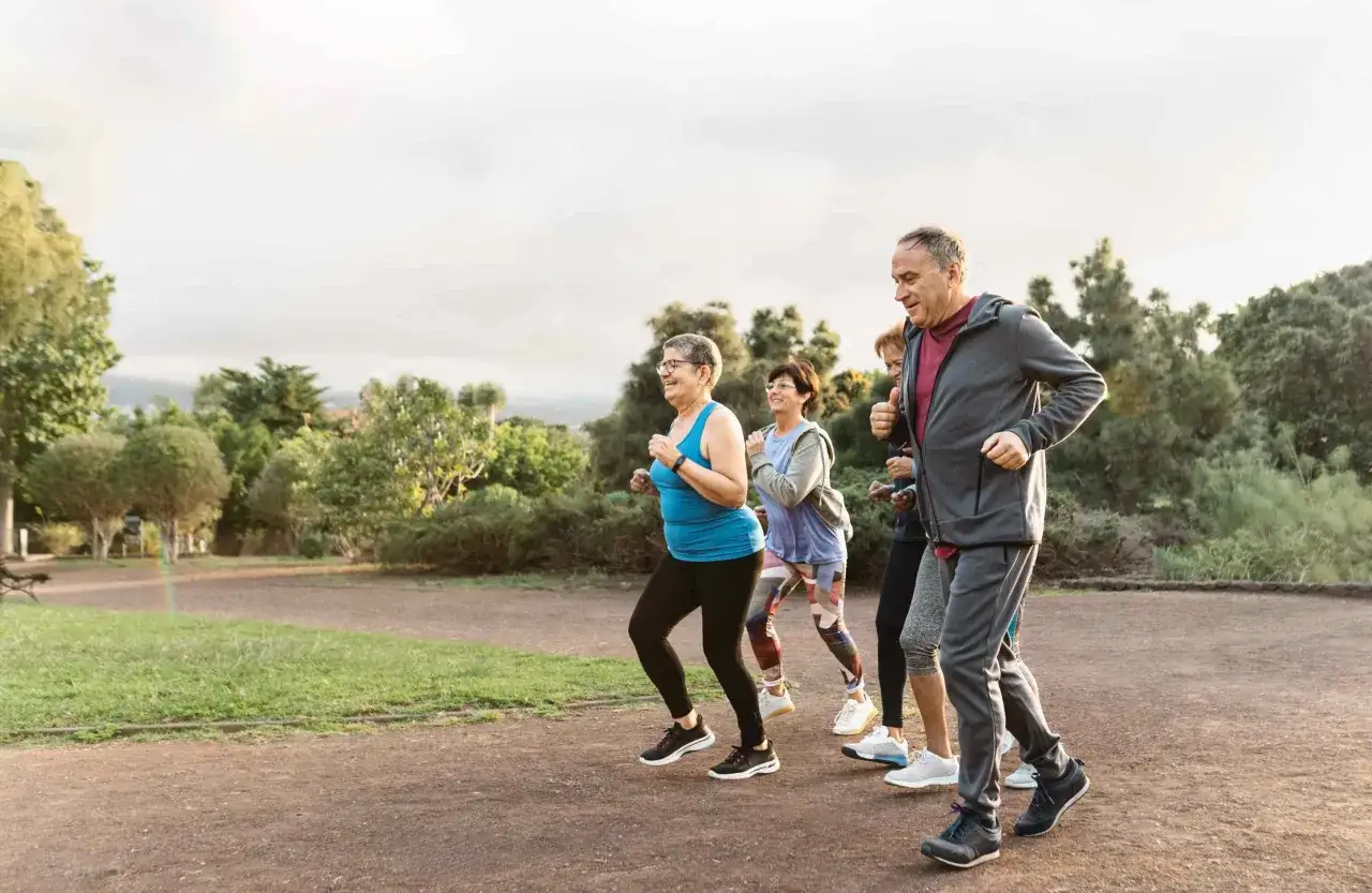 Eine Gruppe &auml;lterer Menschen genie&szlig;t das Laufen im Park. Sie lachen und bewegen sich, was zeigt, was bringt joggen: Freude und Gesundheit.