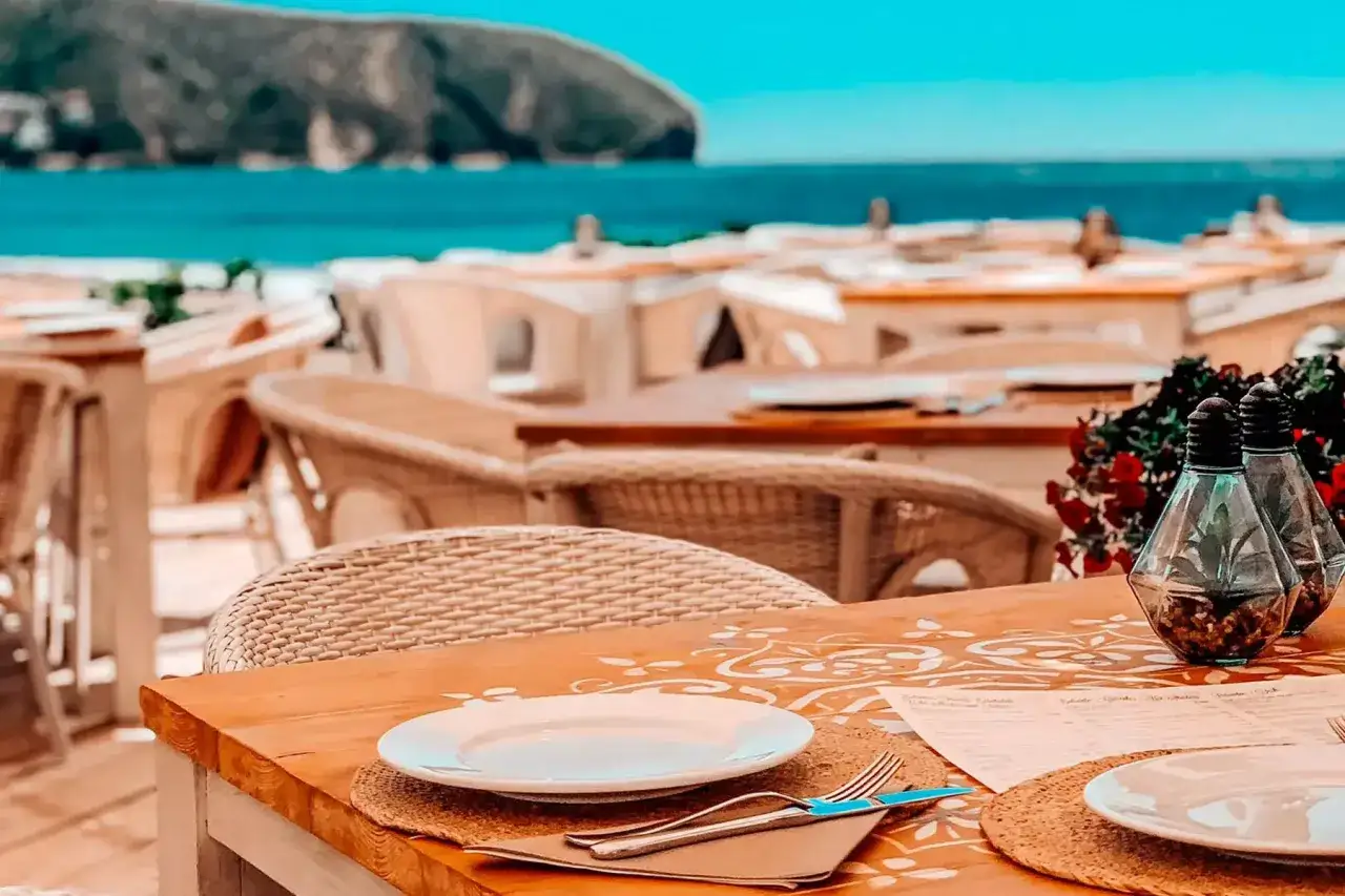 Mesa puesta en un restaurante en Cala Moraig, con vistas al mar y a la montaña. Ambiente playero y relajado.
