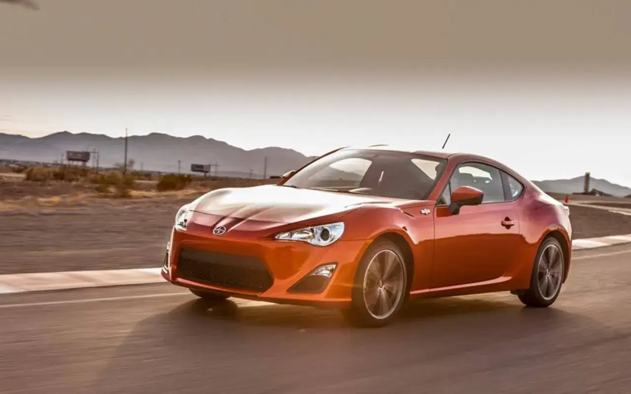 Pomarańczowy Scion FR-S pędzi po torze wyścigowym na pustyni, góry w tle.