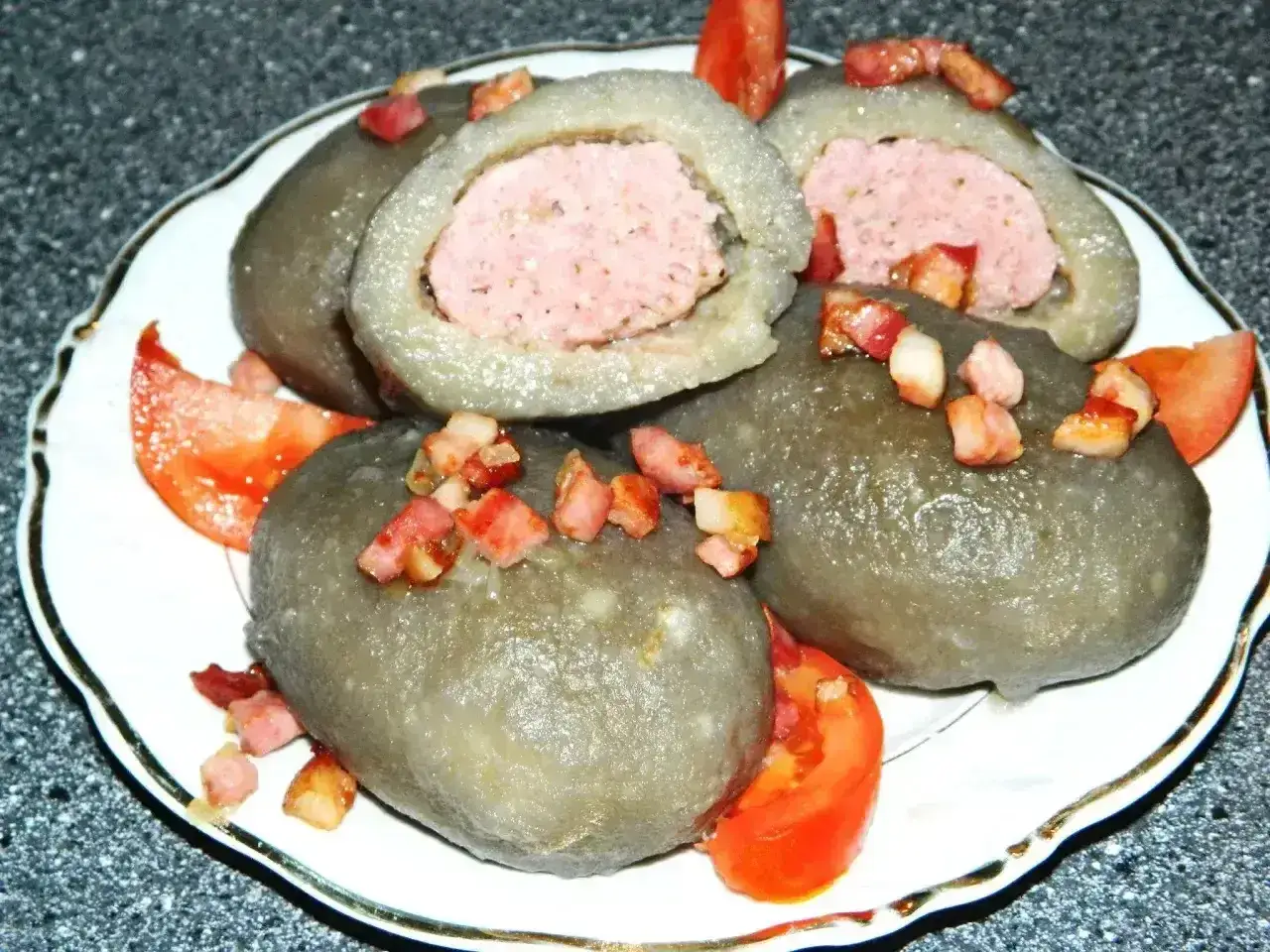 Cepelin z mięsem, polany skwarkami i podany z pomidorem.
