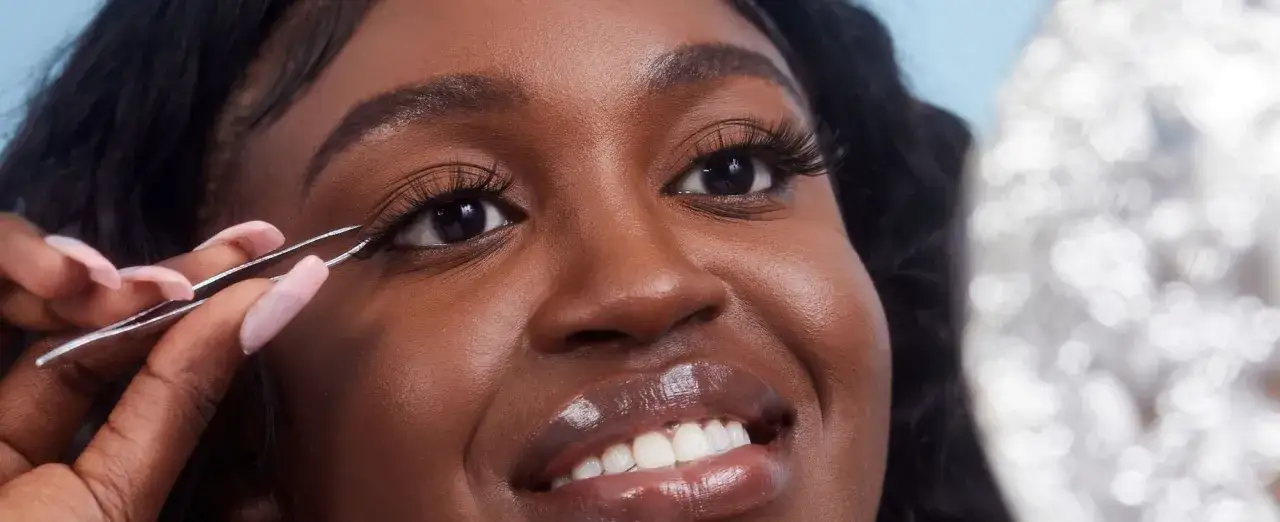 Donna applica ciglia finte con pinzette per un look drammatico. Scopri come mettere il mascara effetto ciglia finte per uno sguardo intenso.
