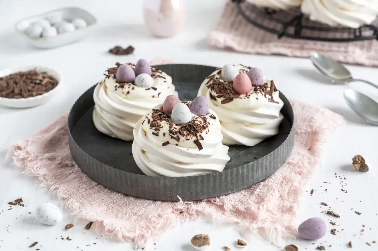 Oster-Pavlovas mit zarter Creme double, Schokostreuseln und bunten Eiern.