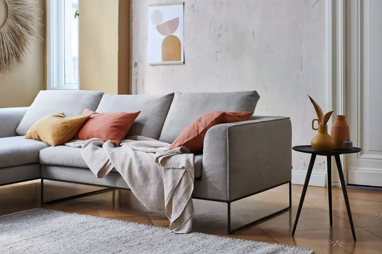 Ein hellgraues Sofa mit Kissen in Rostrot und Senfgelb. Diese Farben passen gut zu Grau und schaffen eine warme Atmosph&auml;re.