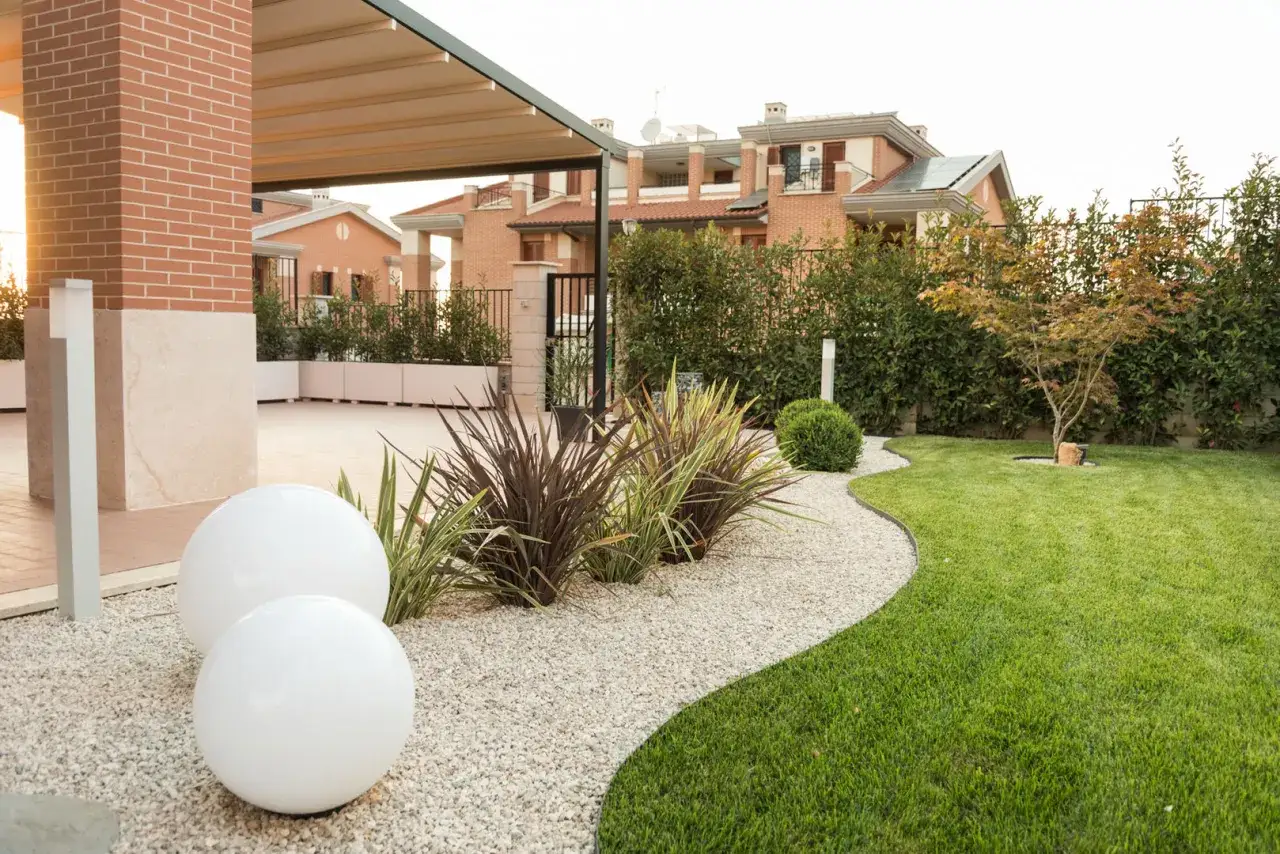 Giardino moderno con ghiaia bianca, sfere luminose e piante esotiche. Idee giardino ingresso casa per un'accoglienza elegante.
