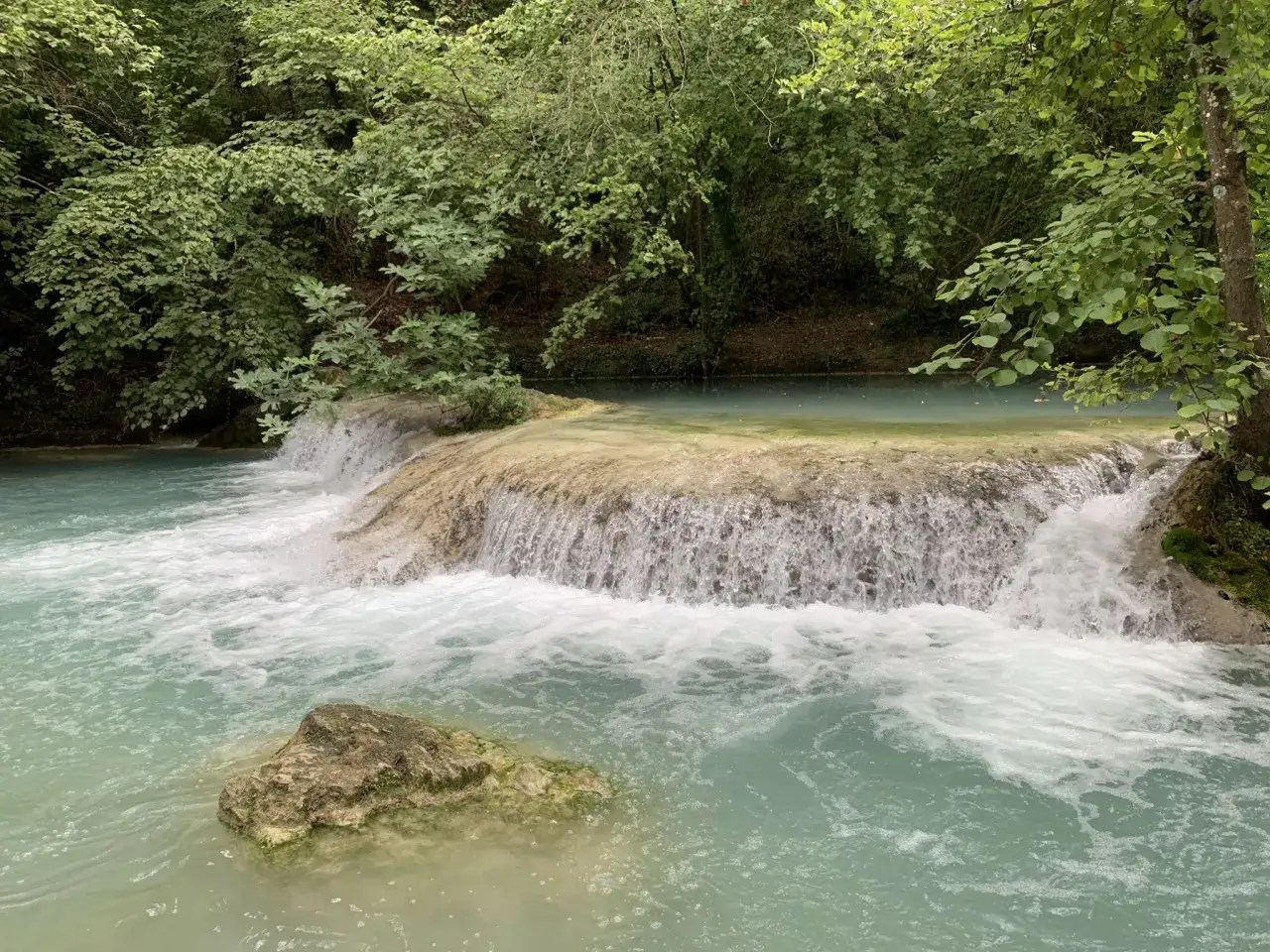 Acqua turchese scorre su rocce calcaree lungo il sentiero delle cascate, circondato da vegetazione lussureggiante.
