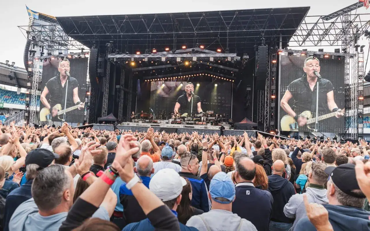 Publiken jublar under en Bruce Springsteen konsert. Stora skärmar visar artisten som spelar gitarr.