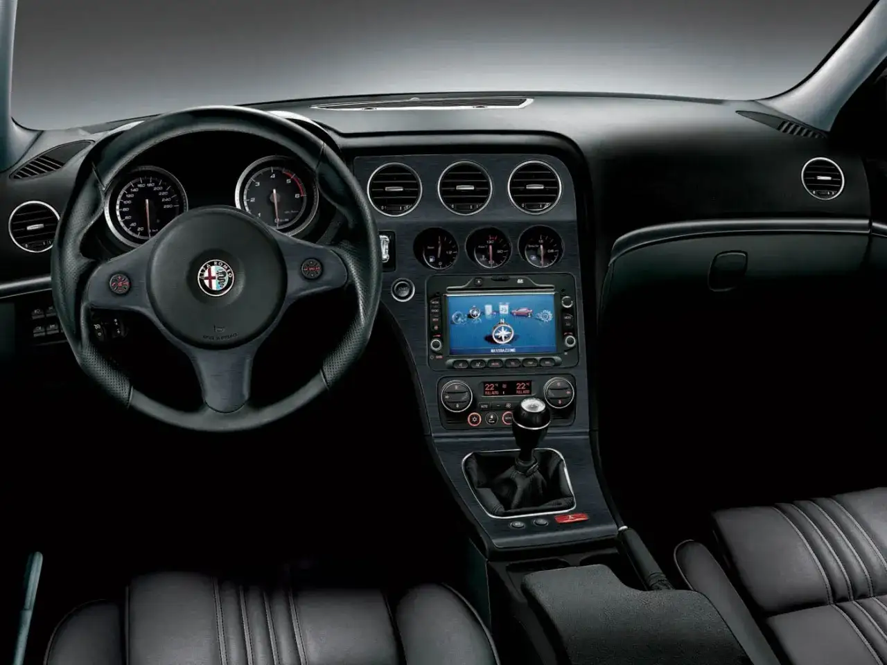 Wnętrze Alfa Romeo 159 2.4 JTDm: kierownica, deska rozdzielcza z nawigacją i zegarami, dźwignia zmiany biegów.