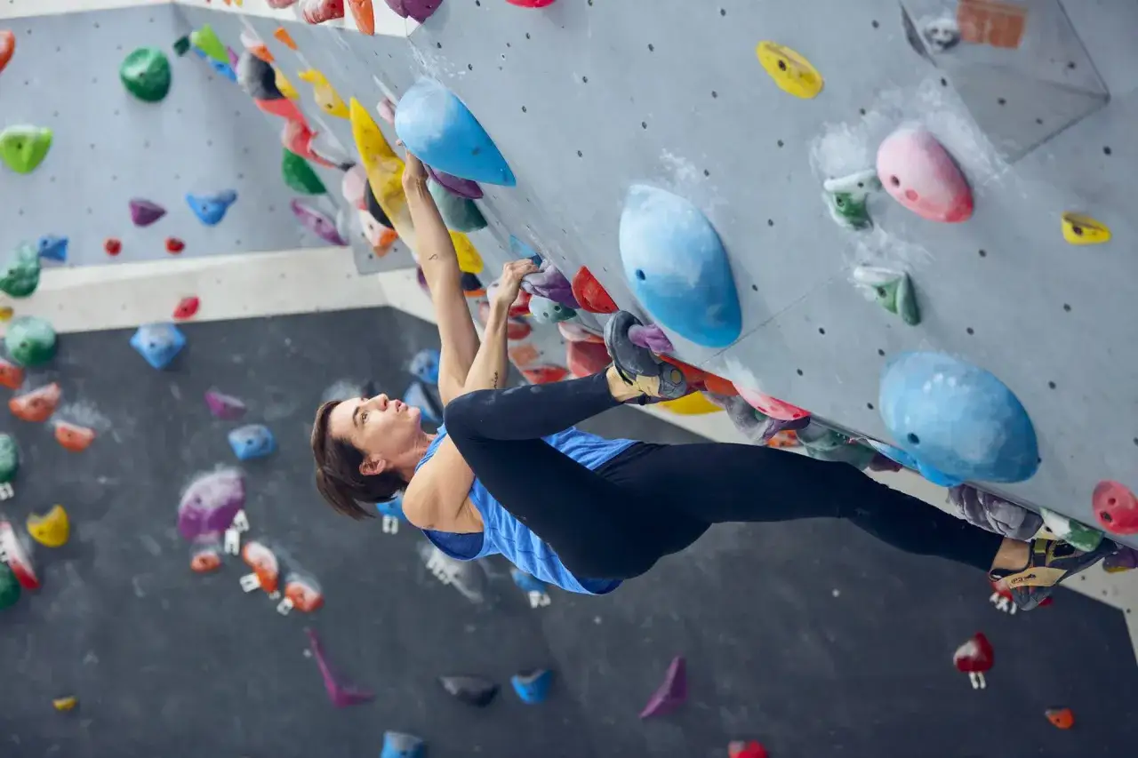 Frau klettert an einer Boulderwand. Sie nutzt verschiedene Griffe, um sich hochzuarbeiten. Hier sind einige bouldern tipps: Füße gut platzieren, Körperspannung halten.