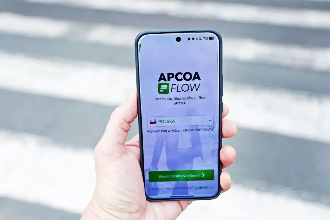 Dłoń trzyma smartfon z aplikacją APCOA FLOW, gotową do bezstresowego parkowania w Polsce.