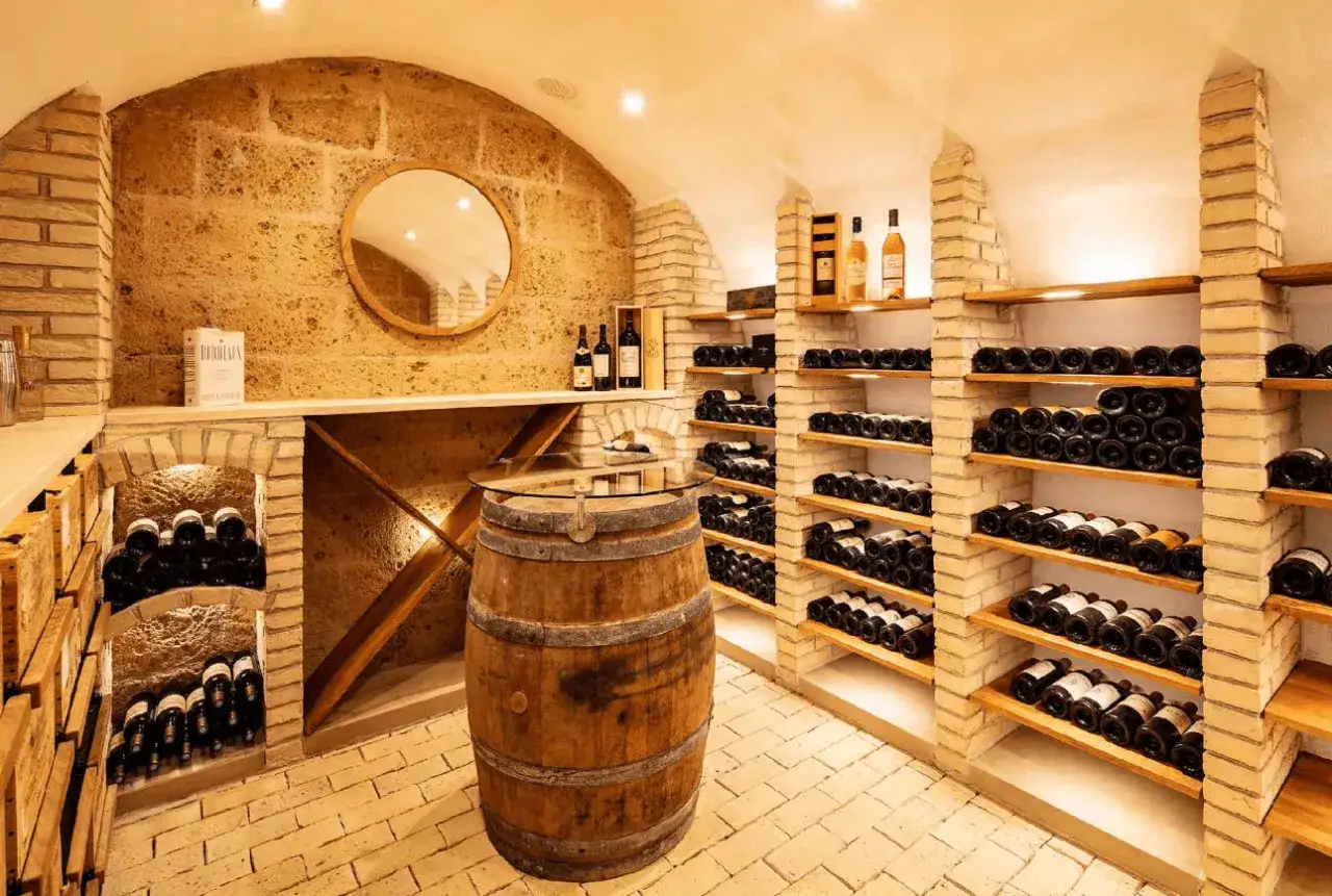Cave à vin parisienne avec étagères remplies de bouteilles, un tonneau et une table en verre. Idéal pour une dégustation vin Paris.