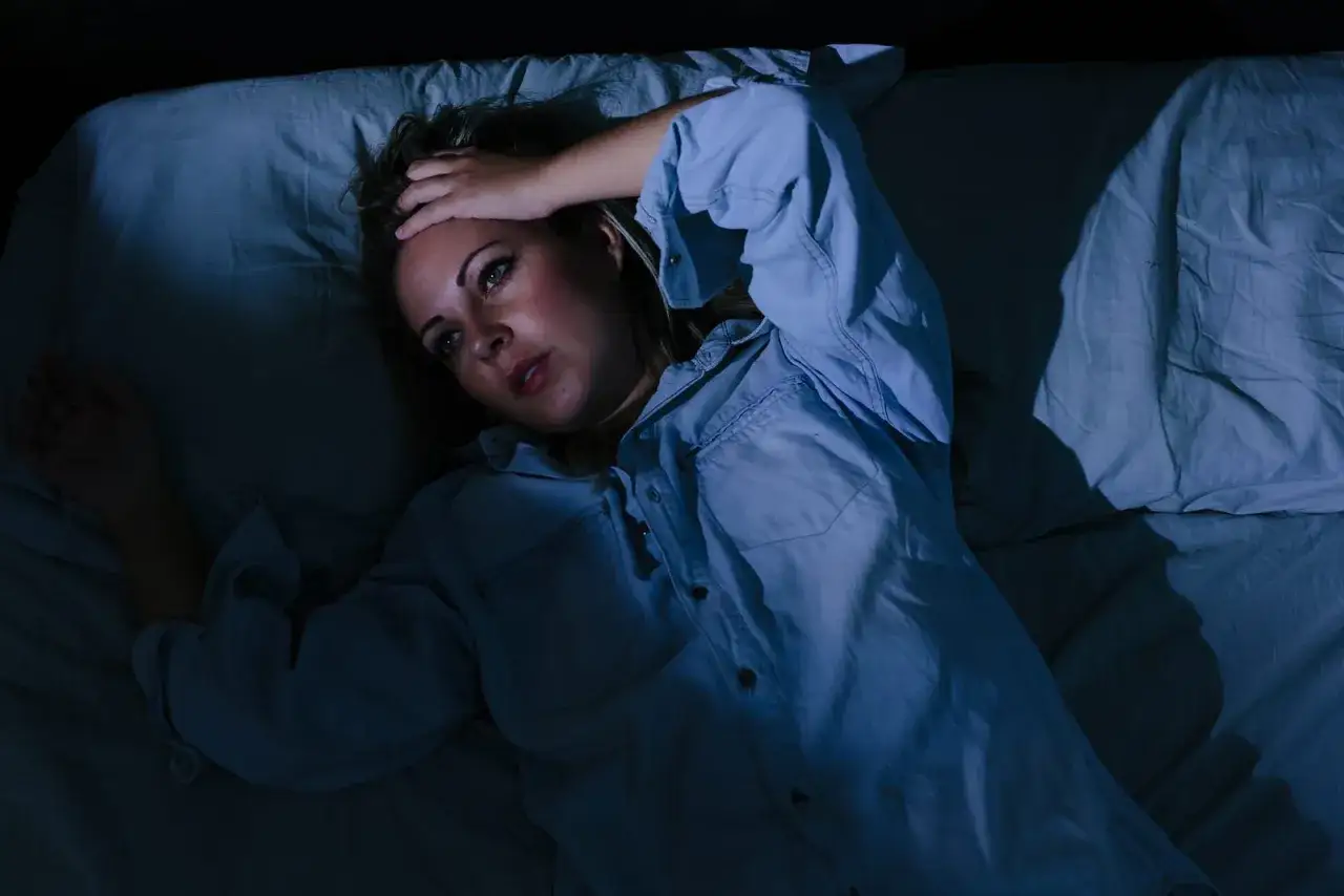 Frau liegt im Bett, hält sich die Stirn. Ihre Augen sind weit geöffnet, sie wirkt besorgt. Ein Bild von stress symptome frau.