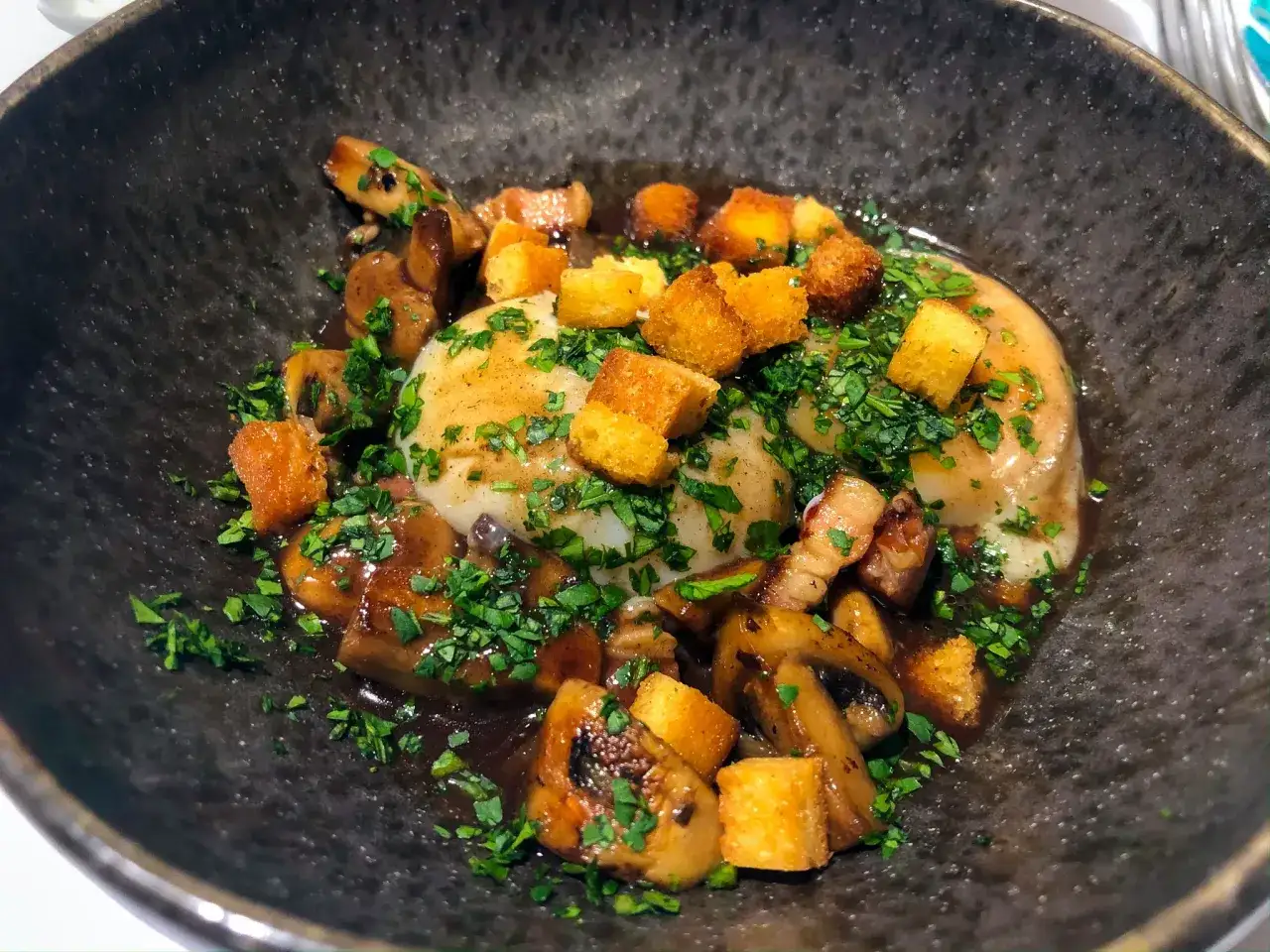 Un &oelig;uf meurette, poch&eacute; et napp&eacute; d'une sauce riche, garni de champignons saut&eacute;s, de lardons croustillants et de cro&ucirc;tons dor&eacute;s, le tout saupoudr&eacute; de persil frais.