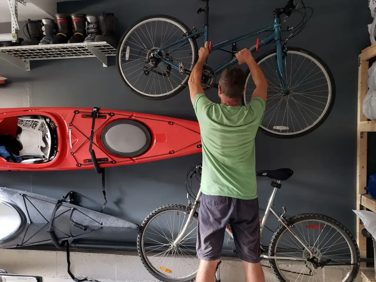Mężczyzna wiesza rower pod sufitem. Obok wiszą kajaki, a na półce buty narciarskie.
