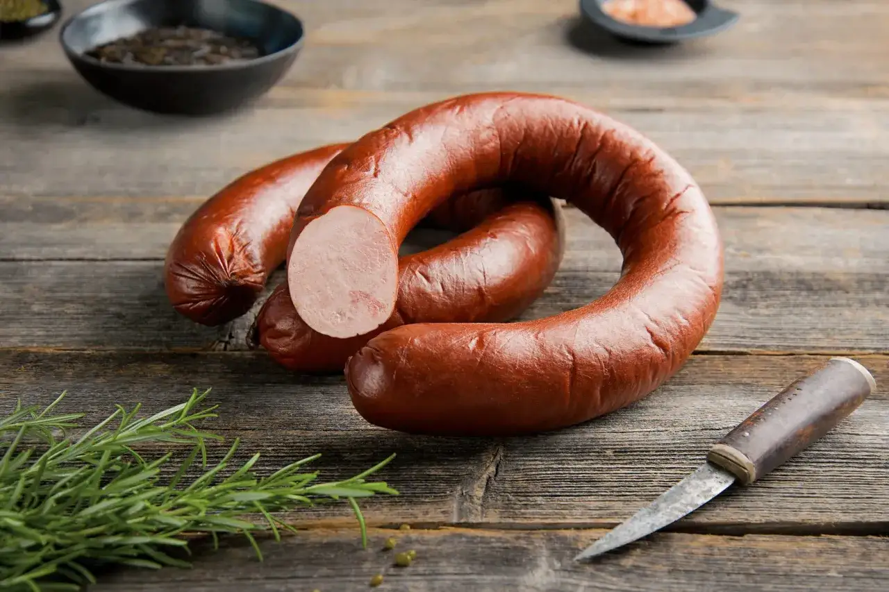 Kiełbasa lisiecka przepis na drewnianym stole. Wędlina, rozmaryn i przyprawy tworzą apetyczną kompozycję.