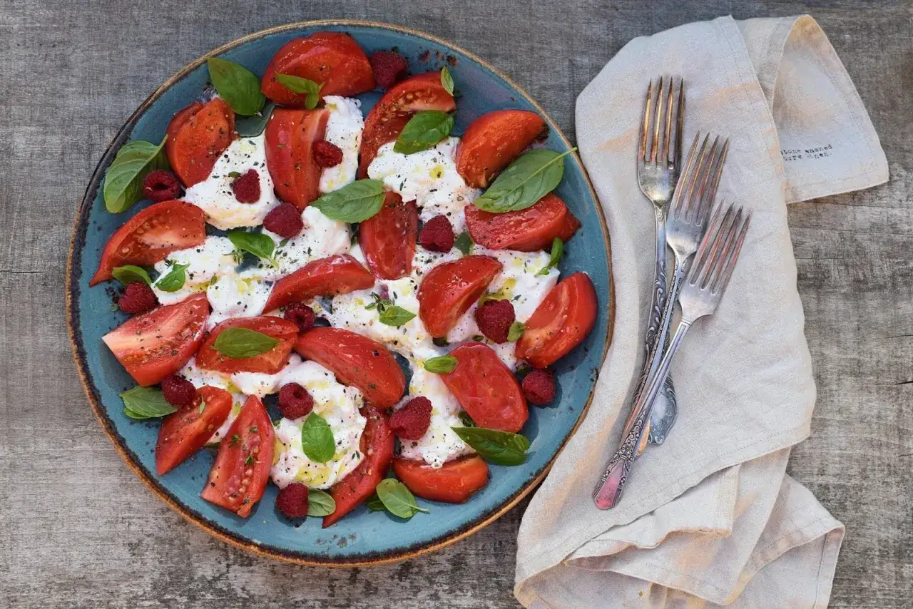 Pyszna burrata z pomidorami, malinami i bazylią, skropiona oliwą. Idealna na letni obiad.