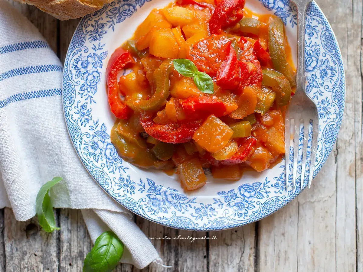 Un piatto di peperonata con patate, colorata e saporita, guarnita con basilico fresco.