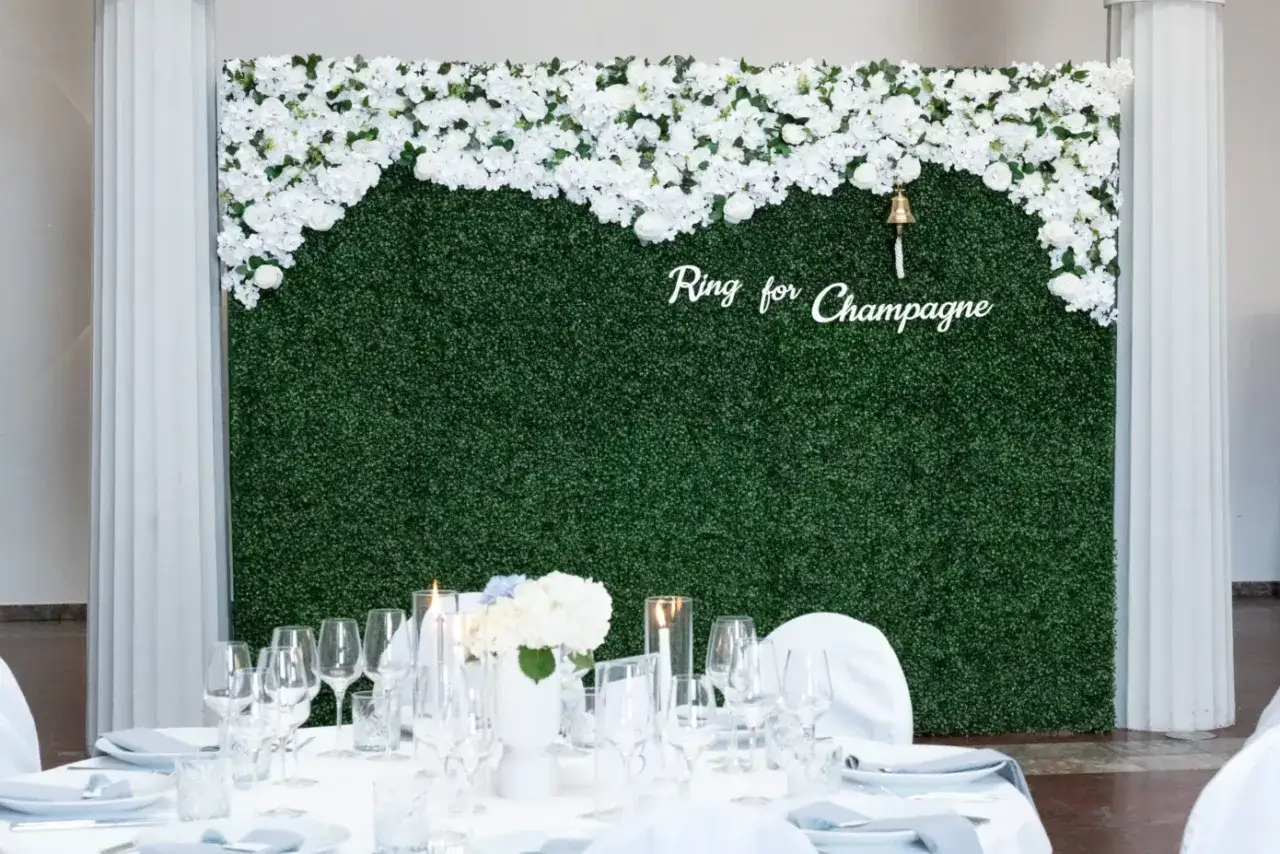 Grüne Wand mit weißen Blumen, darauf ein Glöckchen und die Aufschrift