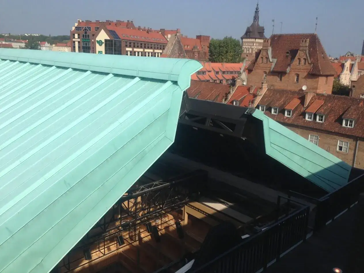 Zielony dach z miedzi nad sceną, w tle zabytkowa zabudowa miasta.