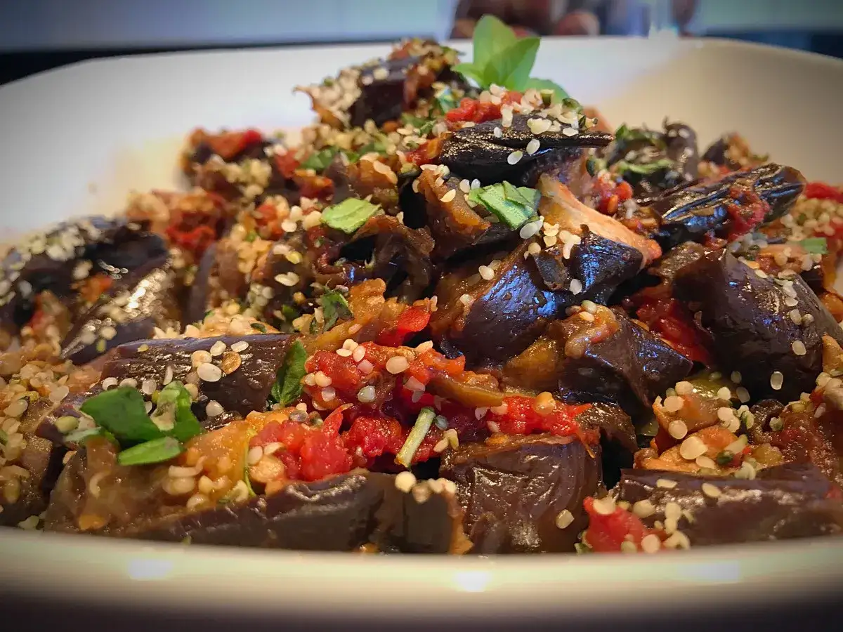 Deliciosa ensalada de berenjenas asadas, con trozos de tomate y semillas de sésamo, decorada con hojas verdes.