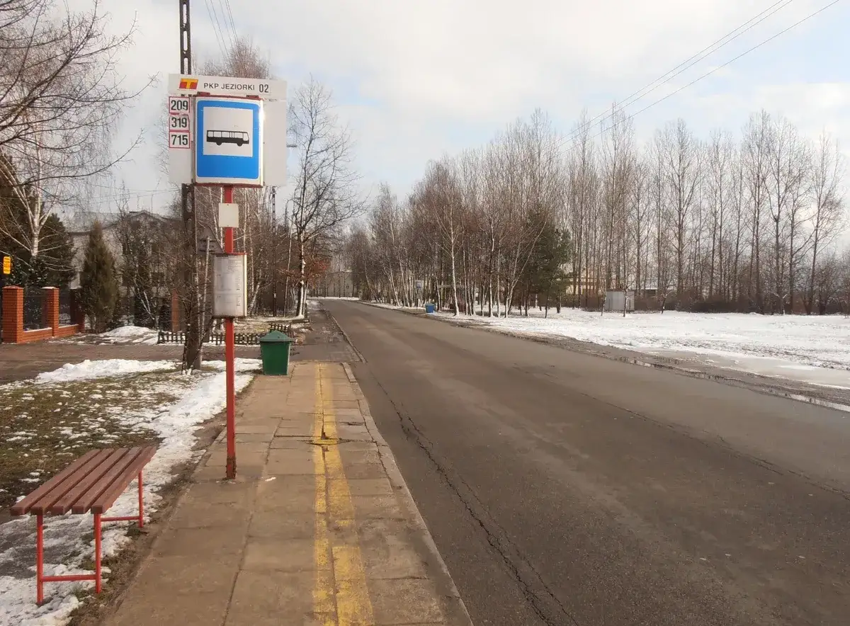 Przystanek autobusowy PKP Jeziorki w Warszawie. Zima, śnieg na poboczu, ławka i pusta droga.
