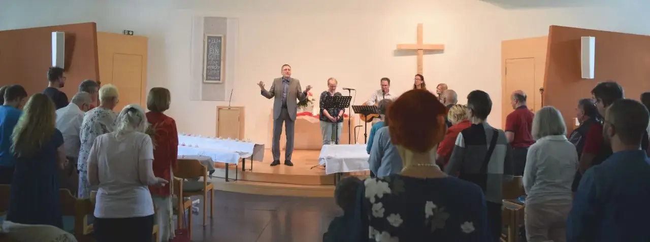 Menschen versammeln sich in einem hellen Raum, um einen Gottesdienst zu feiern. Ein Mann predigt, während andere Musik machen. Dies ist ein Beispiel dafür, was ist eine Freikirche.
