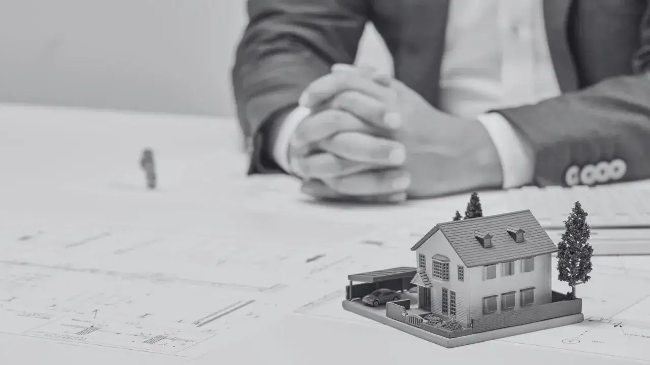 Model domu z garażem i samochodzikiem na tle planów architektonicznych. Biznesmen w garniturze zastanawia się, co wymaga pozwolenia na budowę.