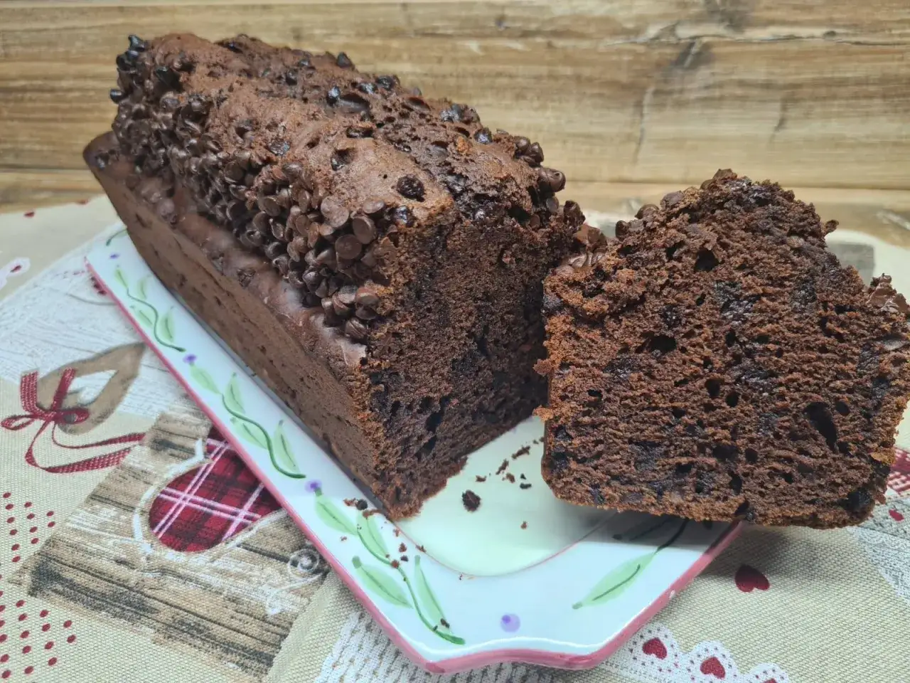 Plumcake al cacao sofficissimo, ricoperto di gocce di cioccolato, su un piatto decorato.