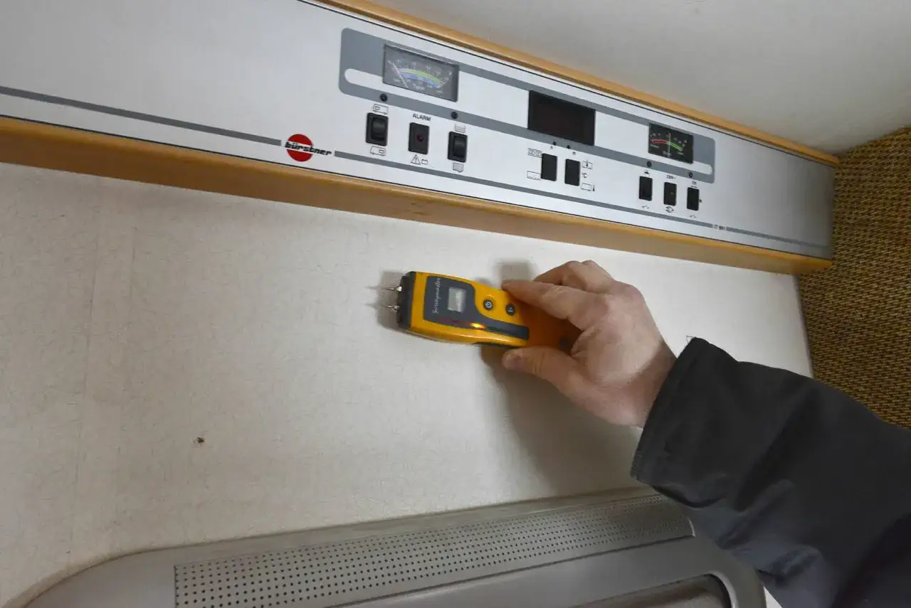 Hand håller fuktmätare mot vägg för fukttest protokoll.