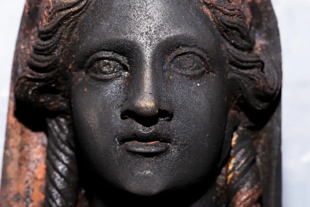 Volto di bronzo antico, forse un reperto del santuario San Casciano dei Bagni, con capelli a trecce e sguardo enigmatico.
