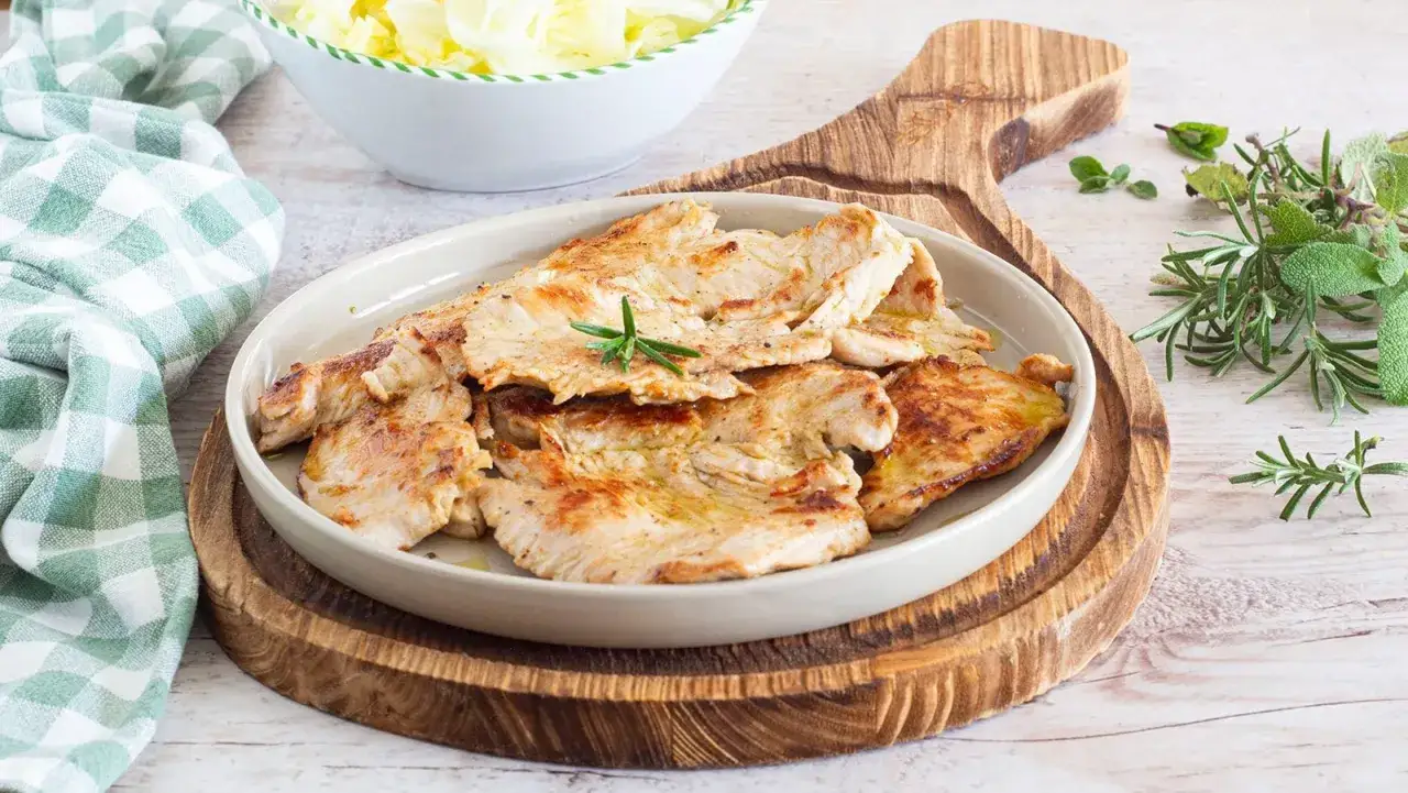 Piatto di fettine di tacchino appetitose, dorate e succulente, guarnite con rosmarino fresco. Accanto, un'insalata croccante e erbe aromatiche.