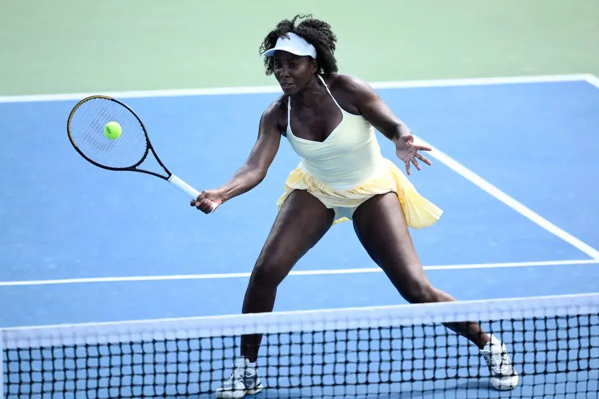 Venus Williams, con su impresionante estatura, golpea una pelota de tenis en una cancha azul.