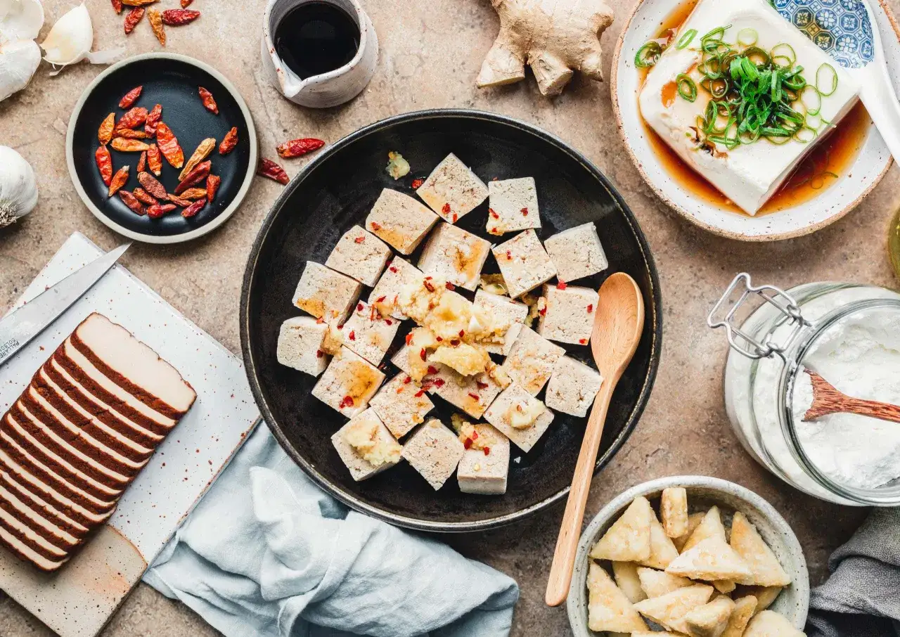 W&uuml;rfel von mariniertem Tofu liegen in einer Sch&uuml;ssel, bereit zum Einfrieren. Daneben liegen Chilis, Knoblauch und Ingwer.