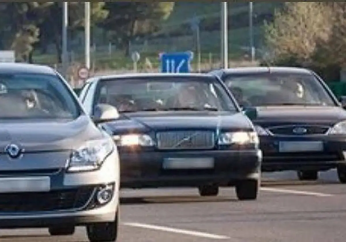 Tres coches en fila en la carretera. El coche del medio, un Volvo oscuro, tiene el alumbrado de posici&oacute;n encendido, iluminando la v&iacute;a.