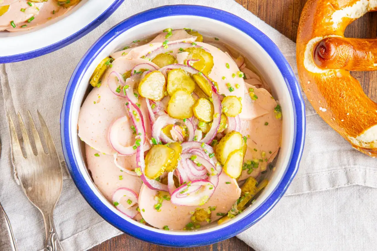 Schmackhafter Wurstsalat mit Gurken, Zwiebeln und Schnittlauch, serviert mit einem Brezel. Das Dressing ist perfekt abgestimmt.