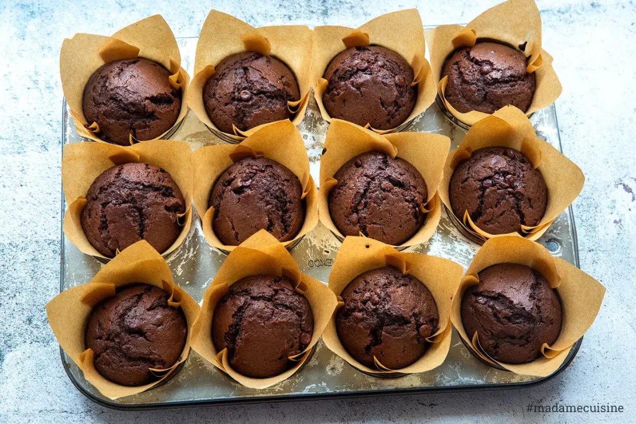 Zwölf saftige Schoko-Muffins in braunen Papierförmchen, bereit für ein einfaches Muffins Rezept.