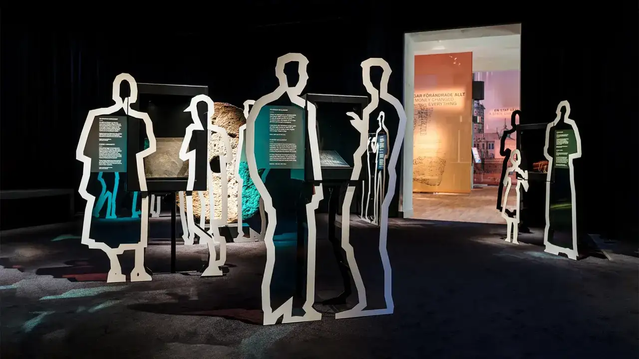 Silhuetter av m&auml;nniskor framf&ouml;r utst&auml;llningar p&aring; ekonomiska museet. En utst&auml;llning visar hur pengar f&ouml;r&auml;ndrade allt.