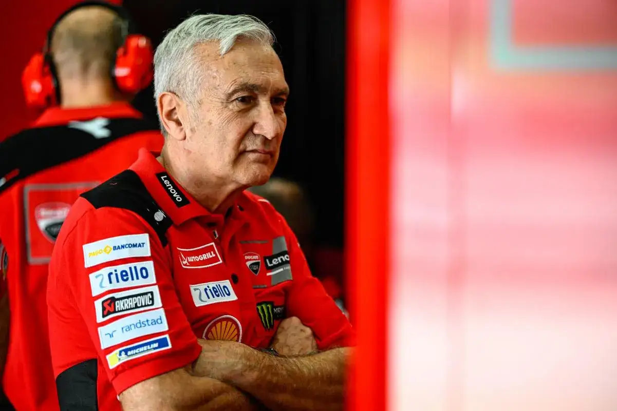 Davide Tardozzi, con brazos cruzados, viste un polo rojo de Ducati con varios patrocinadores.