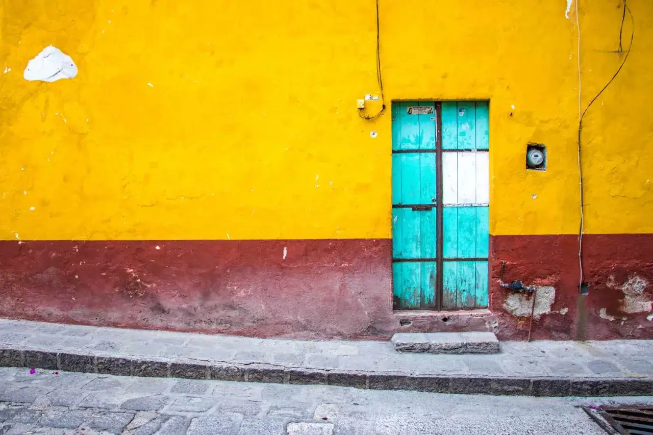Pared exterior amarilla y granate con puerta turquesa. Un ejemplo de cómo pintar una pared exterior en mal estado para darle nueva vida.