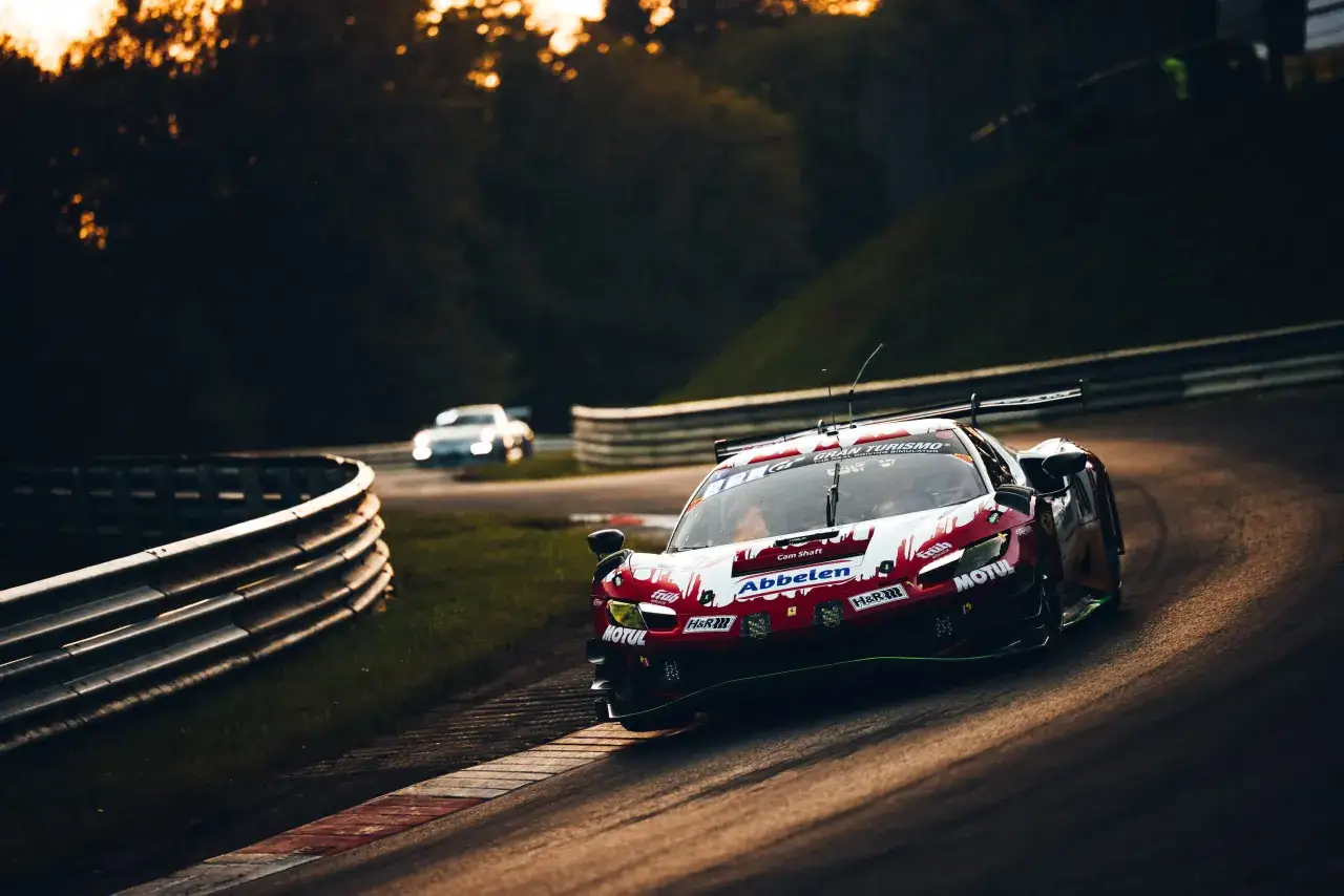 Un coche de carreras rojo y blanco compite en el circuito de N&uuml;rburgring durante las 24 horas.